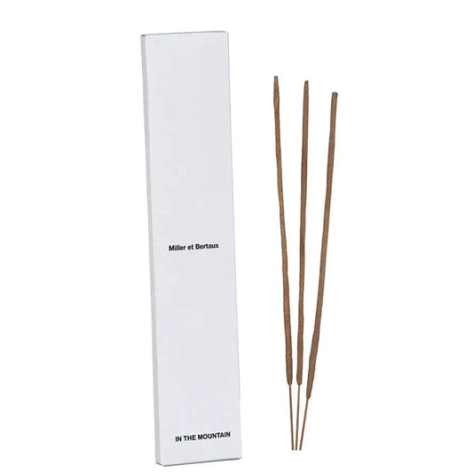 A tall white rectangular box labeled 'Miller et Bertaux' and 'IN THE MOUNTAIN' stands beside three incense sticks white background.