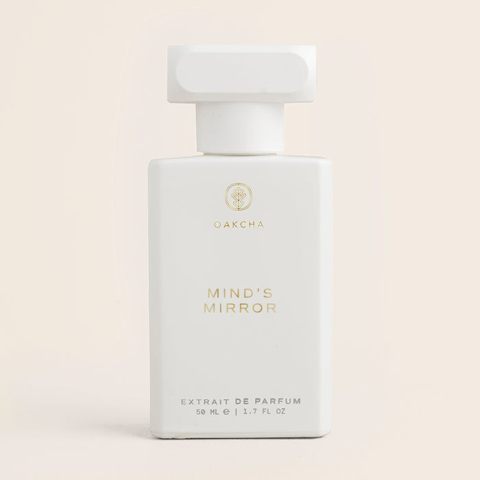 Front view of Mind’s Mirror perfume bottle with white body, T-shaped cap and gold lettering on pale beige background