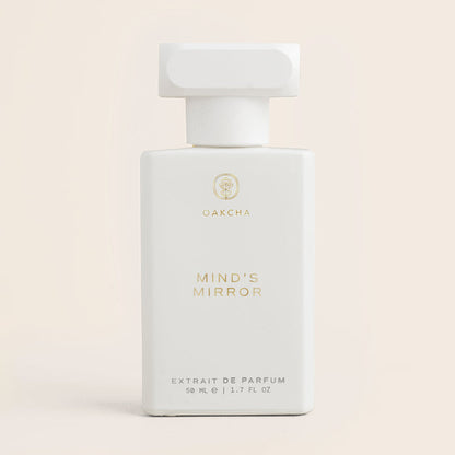 Front view of Mind’s Mirror perfume bottle with white body, T-shaped cap and gold lettering on pale beige background