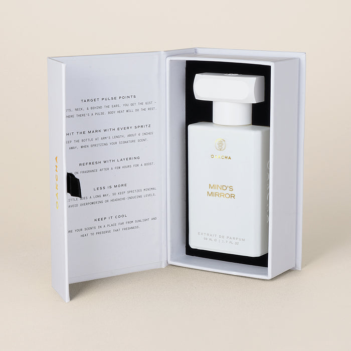 Three-quarter view of Mind’s Mirror perfume bottle inside open white presentation box showing bottle and inner printed panel on beige background
