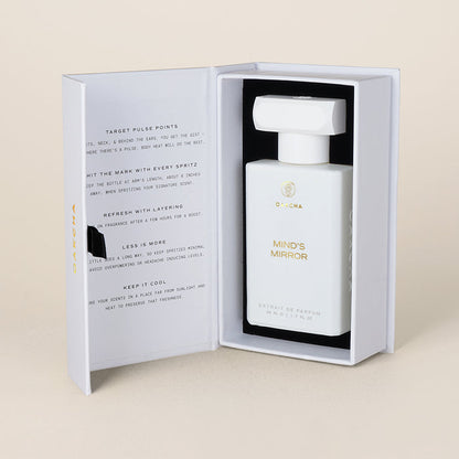Three-quarter view of Mind’s Mirror perfume bottle inside open white presentation box showing bottle and inner printed panel on beige background