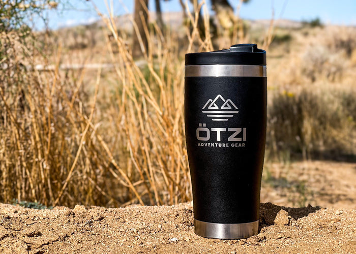 Black Ötzi travel tumbler on sandy ground in a dry outdoor setting