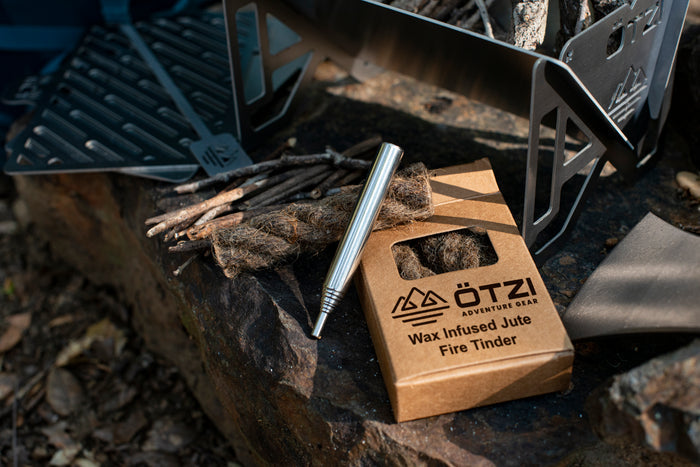 Wax infused jute fire tinder with metal striker next to twigs and a camping stove