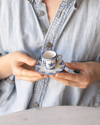 Person holding a tiny tea cup and saucer with blue and white flower details in their hands, showing the small size of the cup.