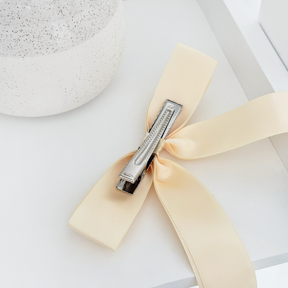 Butter yellow ribbon bow clip on a white surface beside a textured ceramic vase.