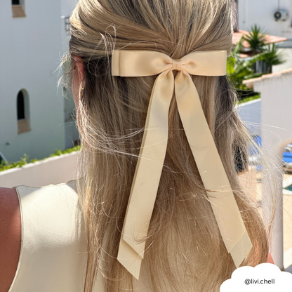 Blonde woman wearing a butter yellow Coconut Lane ribbon bow hair clip, outdoors by white buildings.