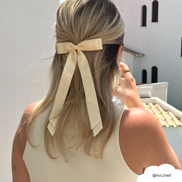 Blonde woman outdoors with hair half up, wearing a butter yellow ribbon bow clip by Coconut Lane.