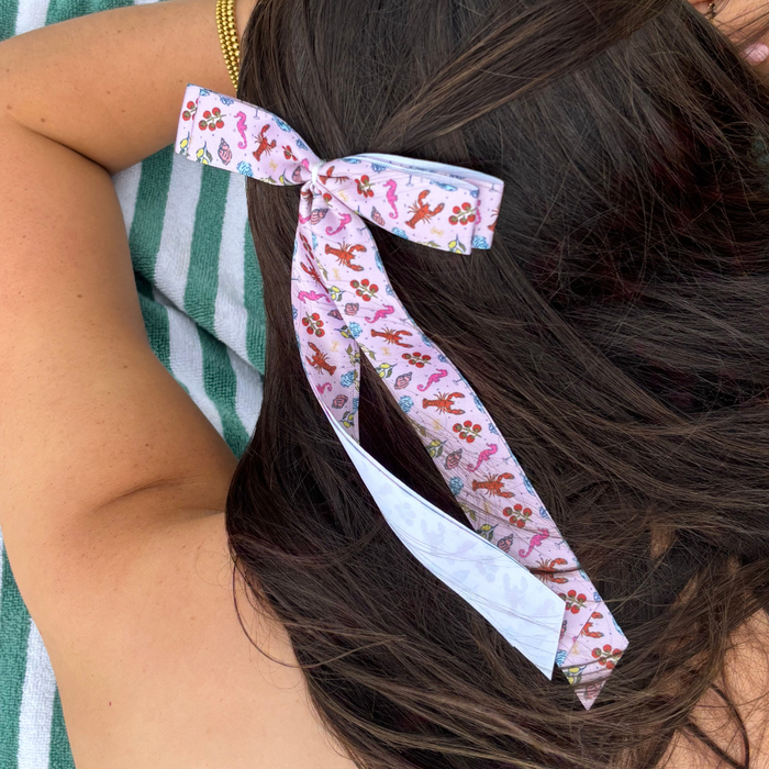 Coconut Lane Cococabana ribbon bow clip in long brown hair beside a green and white striped towel.