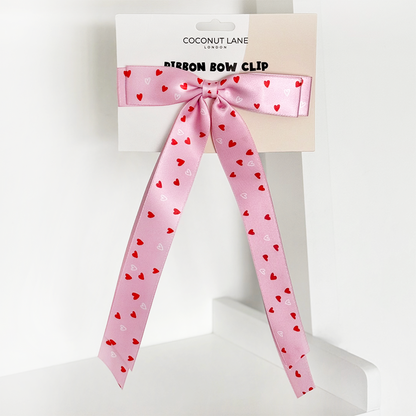 Pink satin ribbon bow clip with red and white heart pattern, displayed on a Coconut Lane branded card.
