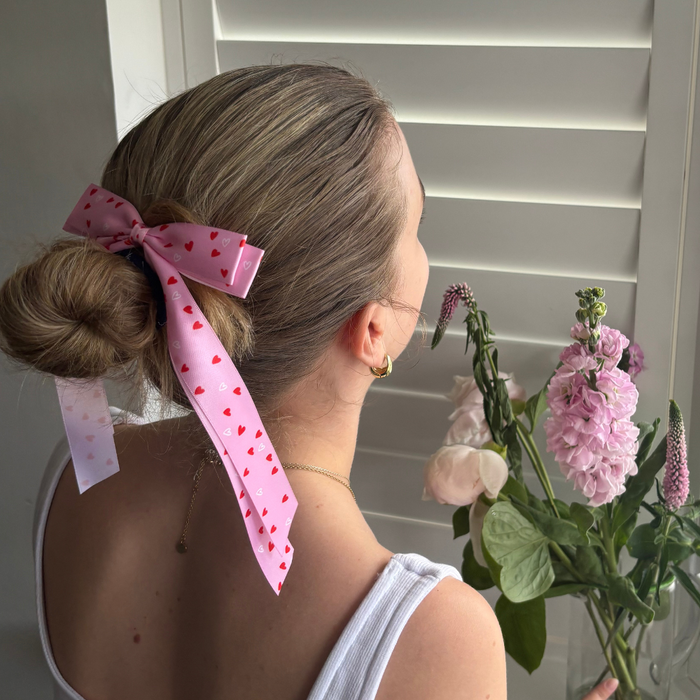 Woman with a Coconut Lane Ribbon Bow Clip featuring a cute heart pattern, holding flowers by white window shutters.