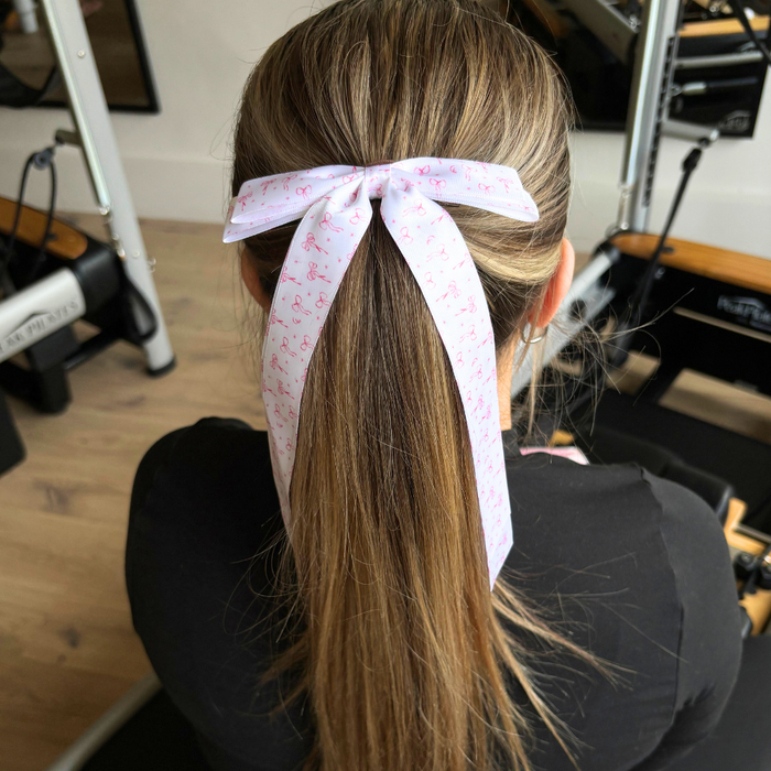 Blonde woman with a ponytail held by a dainty, light-colored ribbon bow clip sits in a gym.