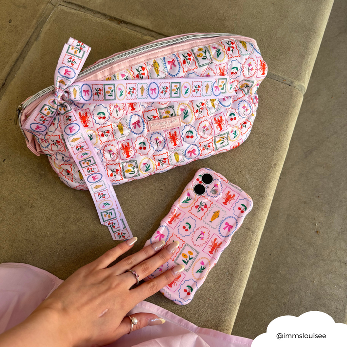 Hand holding a phone with pink floral case next to a satin ribbon bow clip and matching Dolce Vita bag.