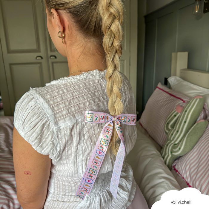 Woman with a long blonde braid wears a light bow hair clip in a cozy bedroom.