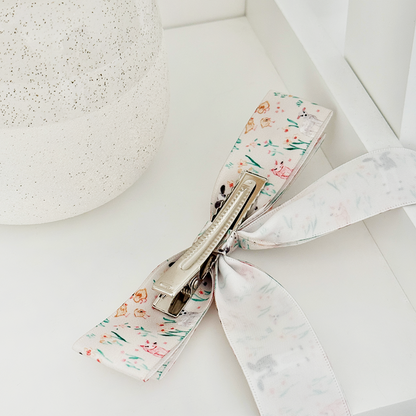 Coconut Lane Ribbon Bow Clip with farmyard print on a white surface next to a textured vase.