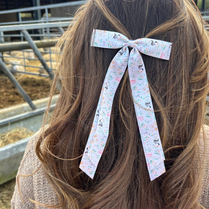 Brown-haired person wearing Coconut Lane Farmyard Friends ribbon bow clip, standing by a metal fence outdoors.