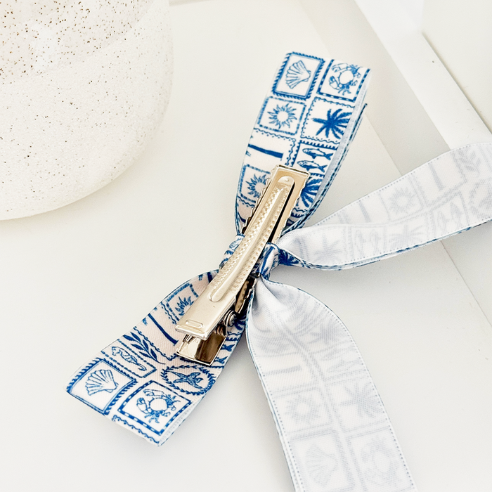 Blue and white Coconut Lane Ribbon Bow Clip on a white surface beside a speckled vase.
