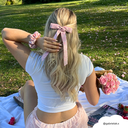 Woman with long blonde hair wears a pink Peony Bow Ribbon Clip, seated on a picnic blanket in a sunny park.