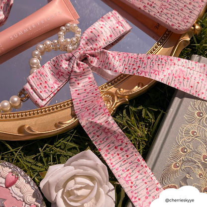 Pink ribbon bow hair clip with pearl bracelet and beauty items arranged on a gold tray with a white rose.