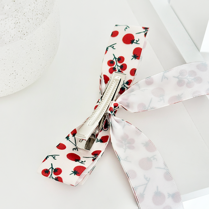 Cherry-patterned ribbon bow hair clip with a secure fastener, featuring vibrant red and green colors.