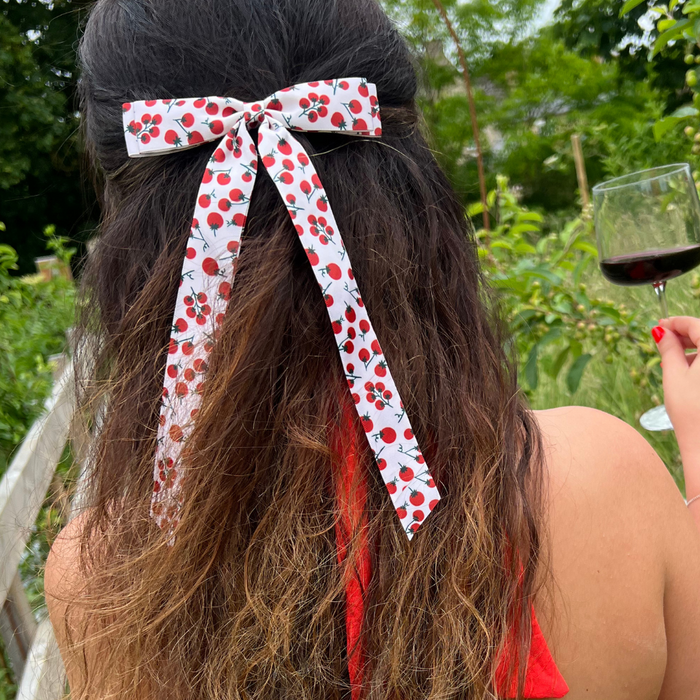 Woman outdoors holding red wine, wearing Coconut Lane Ribbon Bow Clip with a red tomato print.