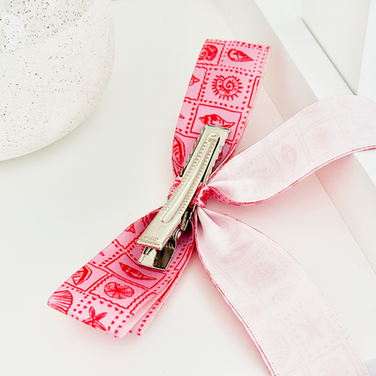 Pink patterned Coconut Lane Ribbon Bow Clip with secure grip, displayed on a white surface.