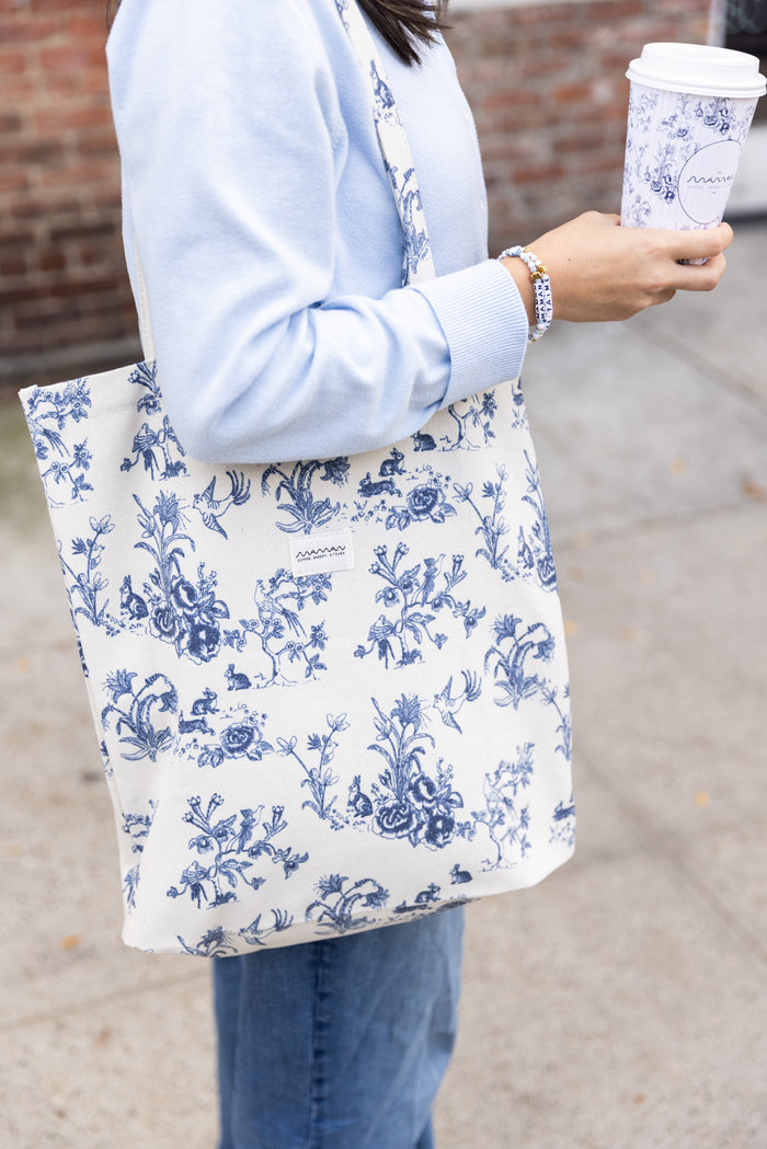 Person holding a tote bag with a blue-and-white floral toile pattern and the maman logo.