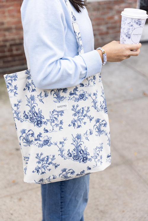 Person holding a tote bag with a blue-and-white floral toile pattern and the maman logo.