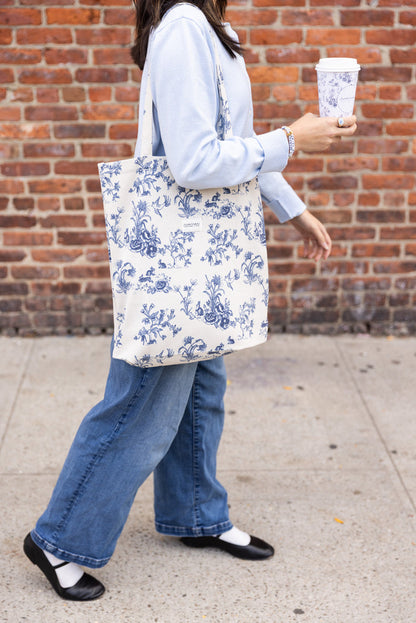 Person holding a tote bag with a blue-and-white floral toile pattern and the maman logo.