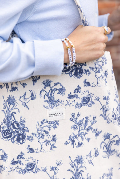 Person holding a tote bag with a blue-and-white floral toile pattern and the maman logo.