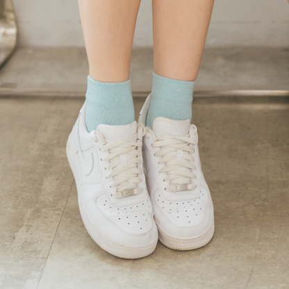 Quarter-length compression socks in light blue worn with white sneakers on a tiled floor.