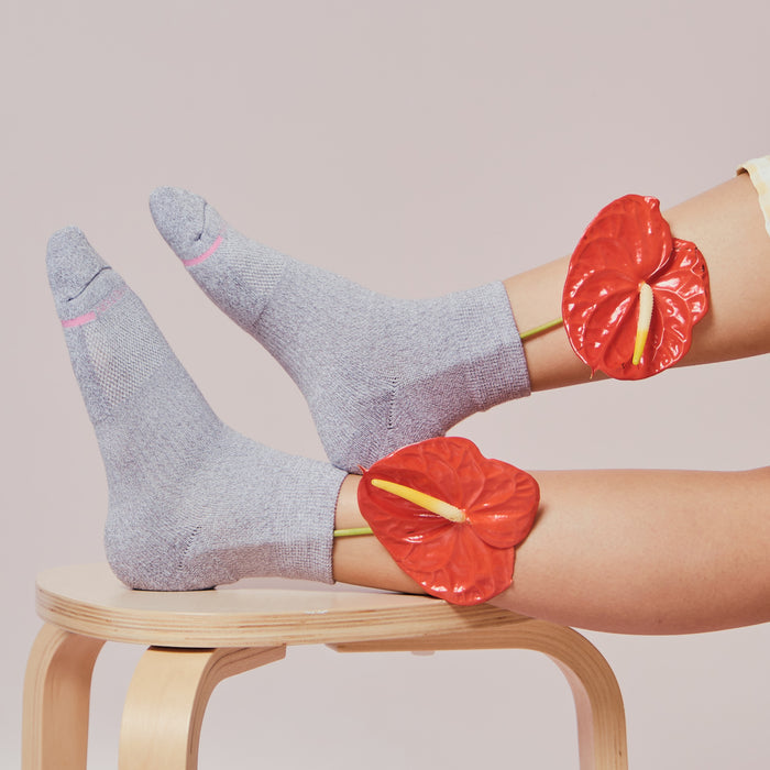 Gray quarter compression socks with pink accents worn on feet, paired with red floral decorations on ankles.