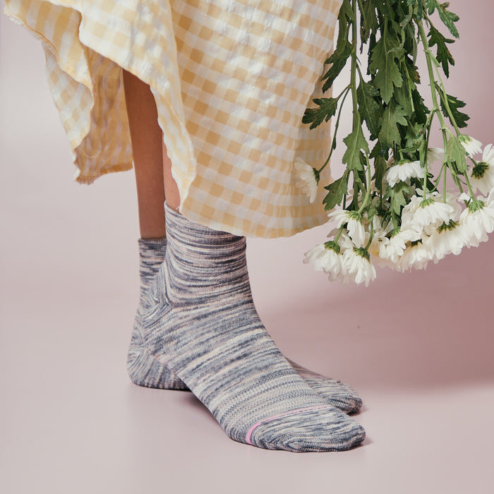 Quarter-length compression socks in a spacedye pattern, worn with a yellow gingham dress and holding flowers.