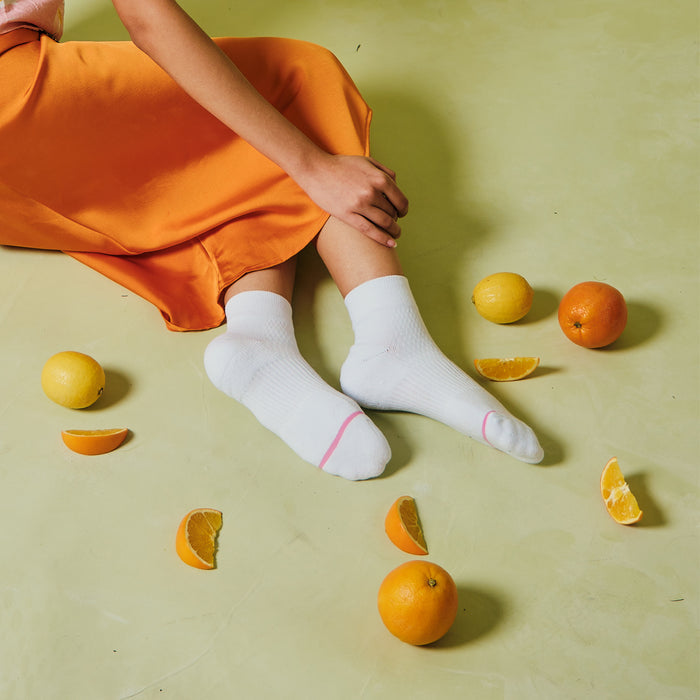 White quarter compression socks with pink accents, worn by a person sitting on a green floor surrounded by citrus fruits.