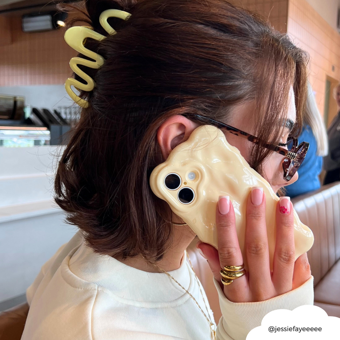 Woman with short brown hair wears a yellow squiggle claw clip and holds a wavy cream phone case.