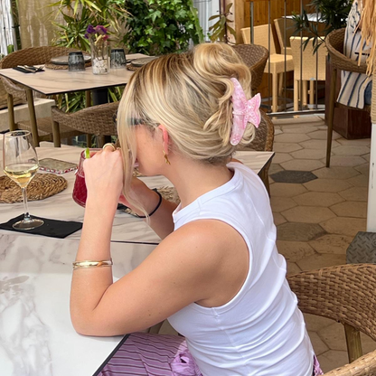 Blonde woman at outdoor cafe wears a pink starfish-shaped hair claw and white top, with a gold bracelet.