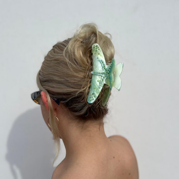 Blonde woman with hair in a bun wears a seafoam starfish-shaped claw clip from Coconut Lane, viewed from behind.