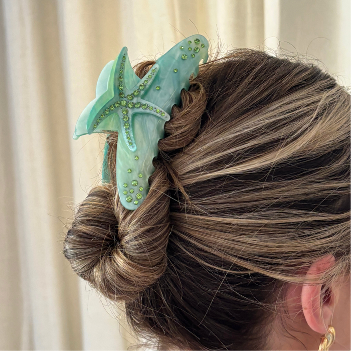 Seafoam green starfish-shaped claw clip with jeweled accents holding a womans hair in a bun.