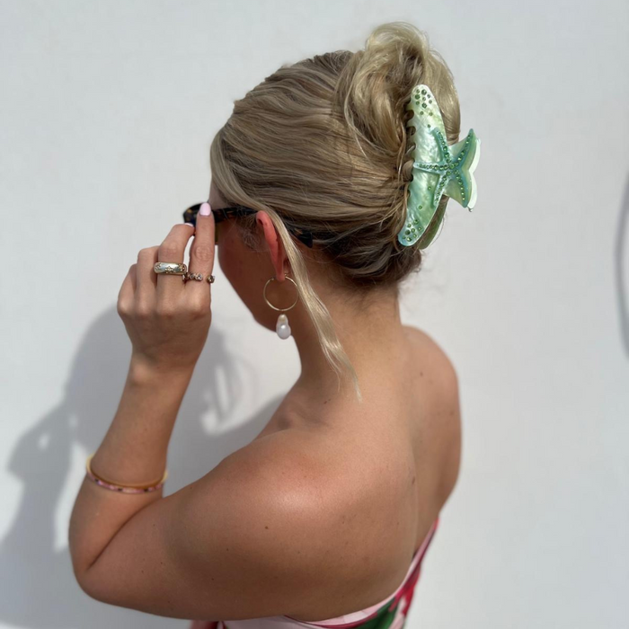 Blonde woman facing away wearing a seafoam starfish-shaped hair claw, sunglasses, and hoop earrings.