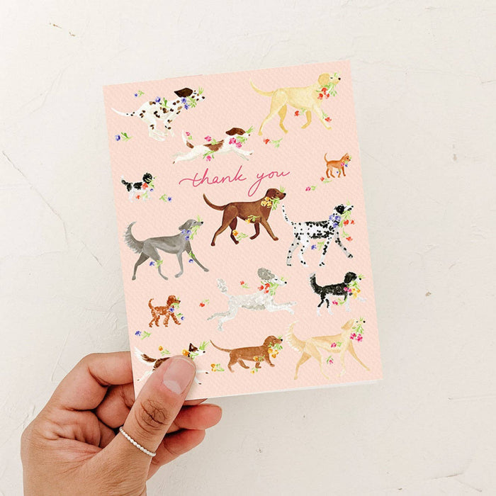 Card with dog illustrations and 'thank you' text held by a hand on a light background