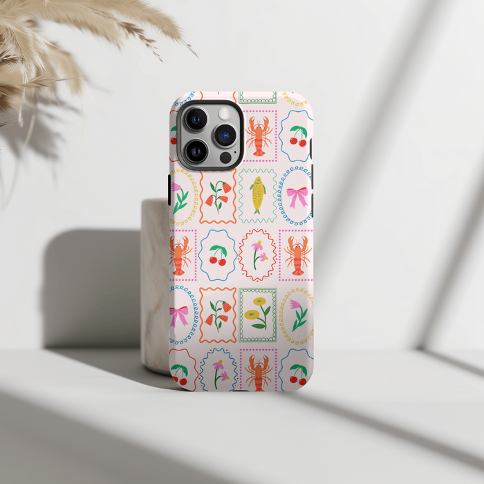 IPhone in Coconut Lane’s Tough MagSafe case with a colorful lobster and floral pattern on a sunlit surface.