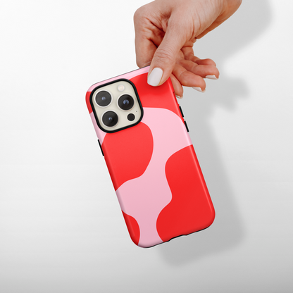 Hand holding a phone with a red and pink cow print case on a light gray background