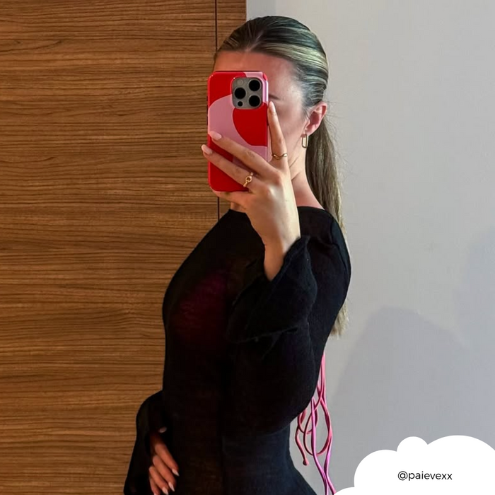 Woman holds a red phone with an abstract pink and red Coconut Lane tough case, taking a mirror selfie.