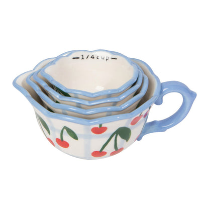 Set of four ceramic measuring cups with cherry design on a white background