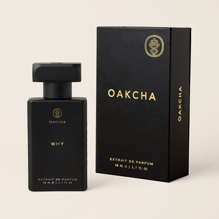 Front-facing view of Why extrait de parfum bottle and matching box showcasing matte black finish and gold lettering on a light beige background