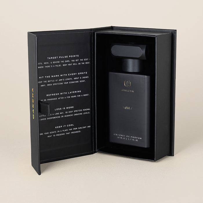 Front view of Why Extrait de Parfum bottle inside open black presentation box showing printed interior text on a beige background